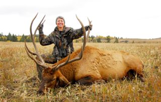 Idaho Elk Hunt: A woman smiles while holding the antlers of her trophy elk.